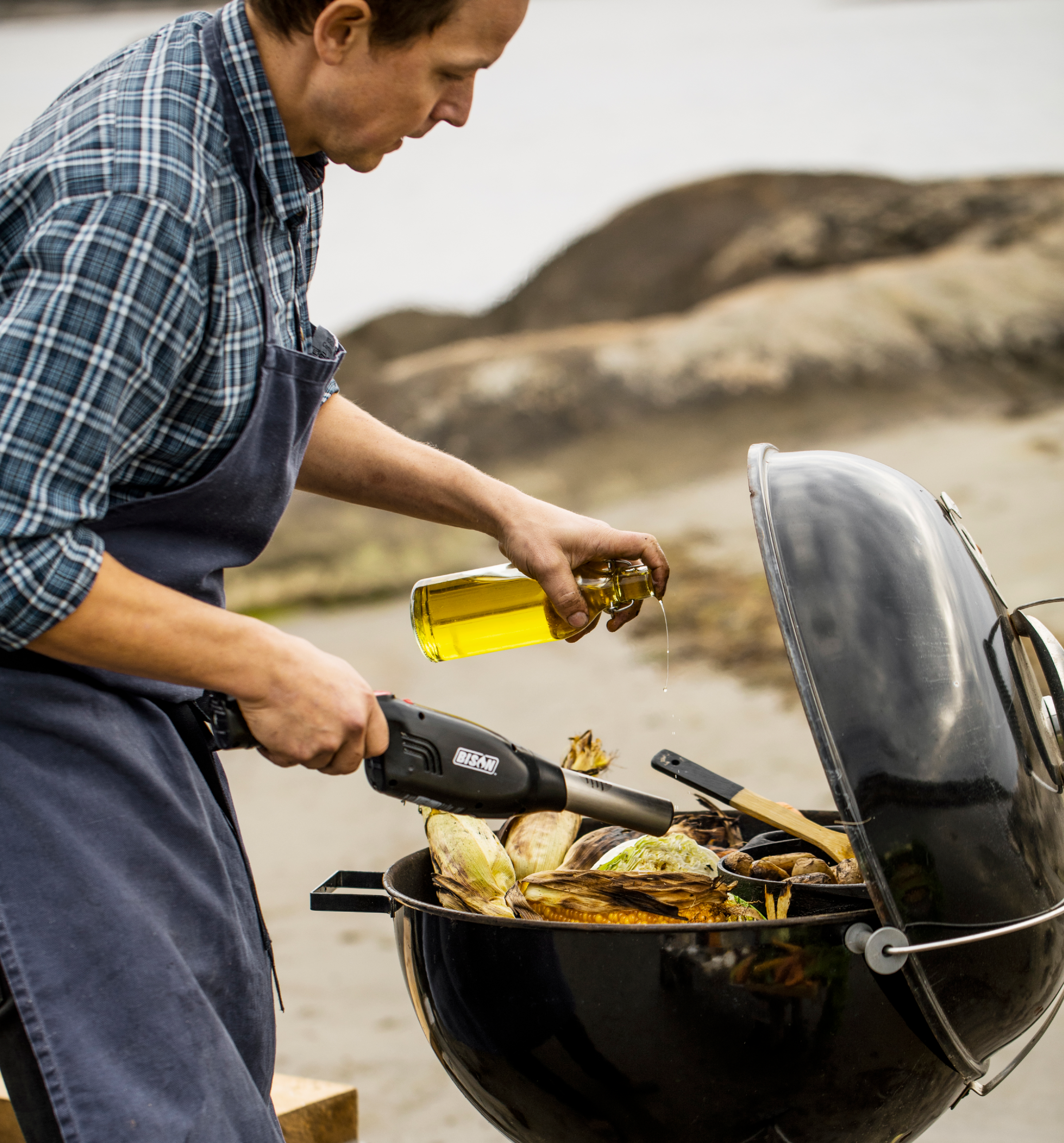 Man using Airlighter and pouring olive oil on corn in the grill.