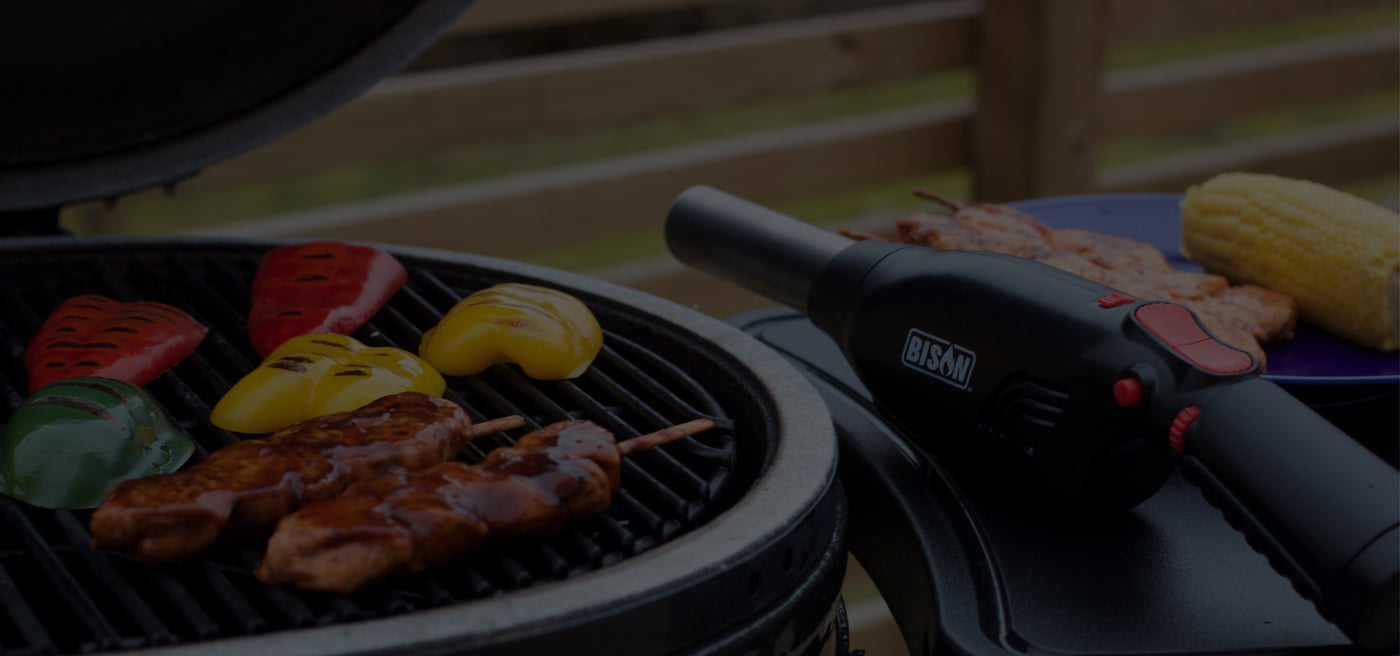 The Bison Airlighter® 420 placed next to a charcoal grill with sizzling vegetables and skewers, highlighting a fast and chemical-free way to start BBQs.