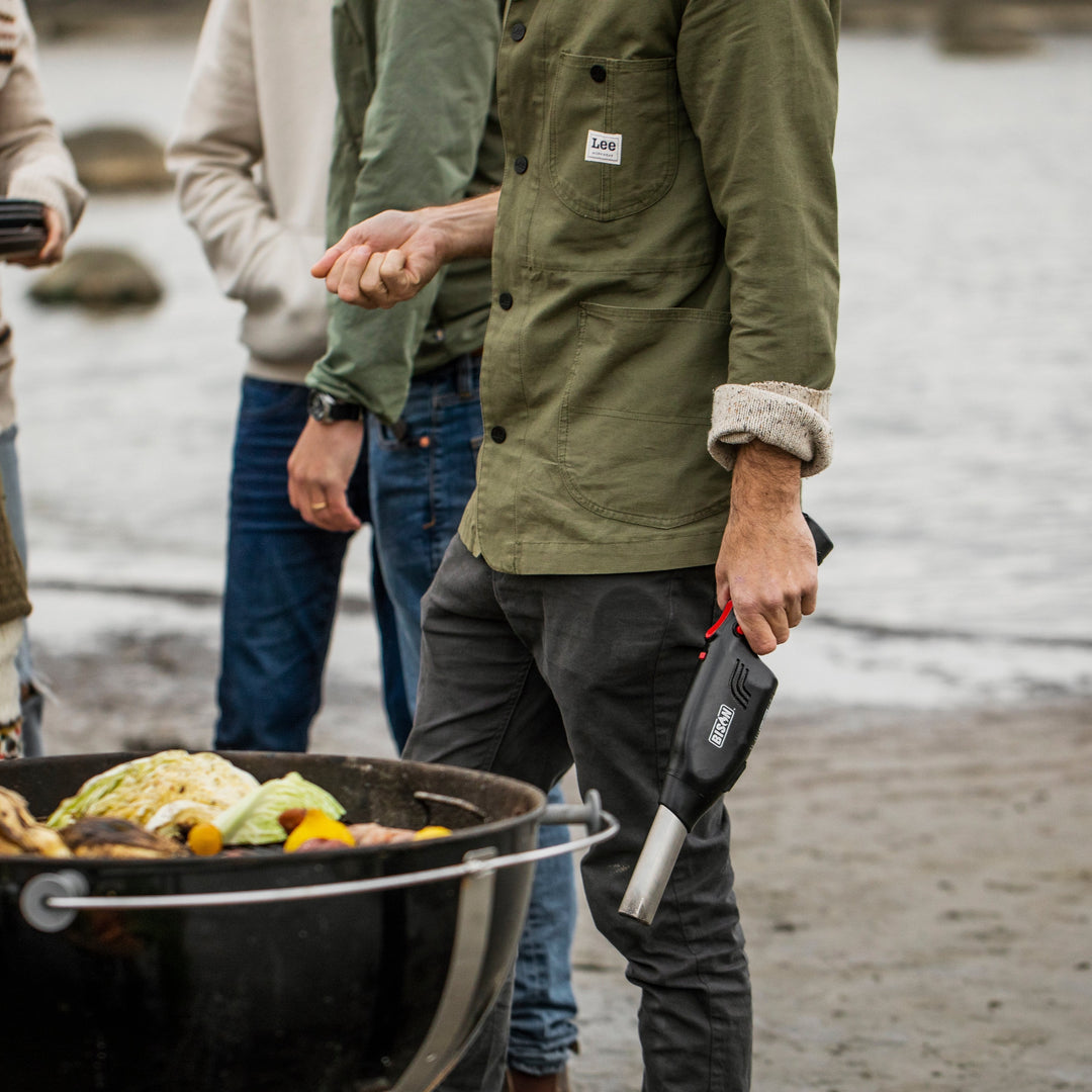 Man using Bison Airlighter to light a grill during an outdoor beach barbecue.