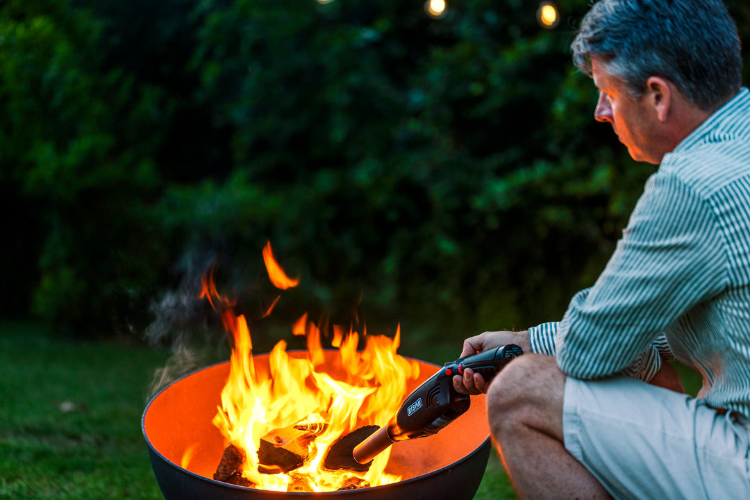 Man lighting outdoor fire pit with an airlighter in a backyard garden